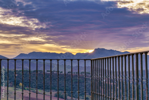 view of a sunset in a mountain landscape with dramatic and colorful cloudy skies seen from a lookout point with a metal railing