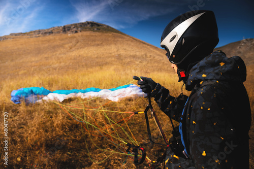 paraglider lands or rises on the yellow grass on a sunny day. A man after or before a paragliding flight. Glider with parachute, wide angle rear view