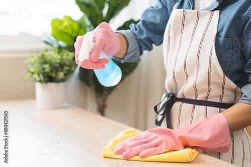 Cleanliness asian young woman working chore cleaning on table at home, hand wearing glove using rag rub remove dust with spray bottle. Household hygiene clean up, cleaner, equipment tool for cleaning