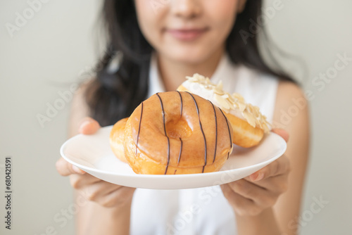 Close up donut plate with happy smile asian young woman, girl temptation food, enjoy eating sugar glazed doughnut and delicious dessert sweet, snack tasty. Eat fast food, junk food meal getting fat. photo