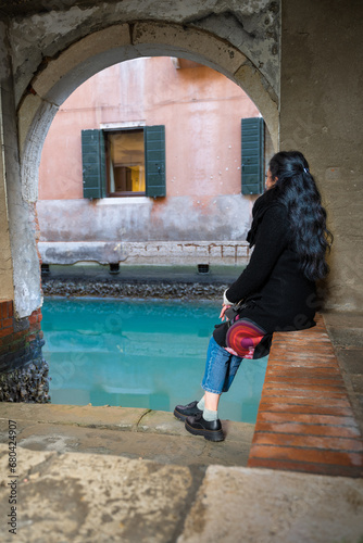 Venetian glimpse with silky water and lagoon colours. Smiling and sitting woman with long hair © Tommaso