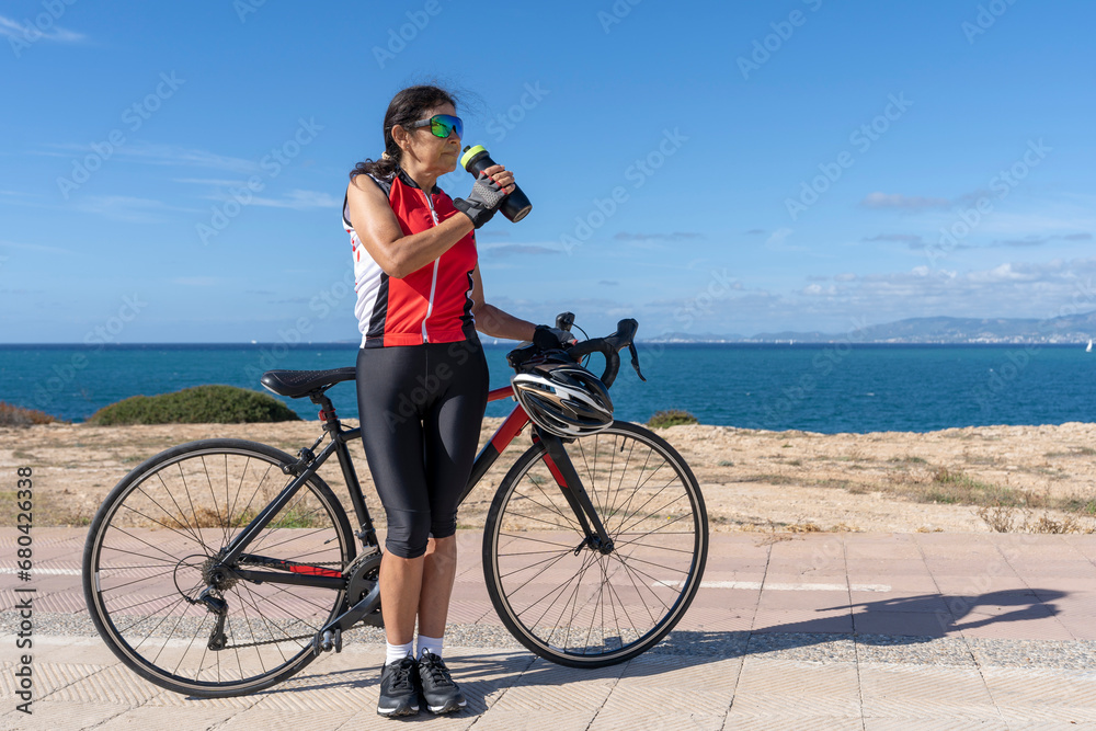 Fototapeta premium Cyclist woman drinking water next to her bicycle. Concept of sporty, active, happy woman