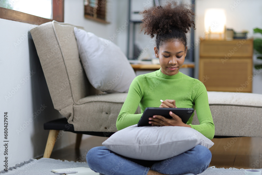 Obraz premium Beautiful african woman in living room using tablet while relaxing on sofa at home.