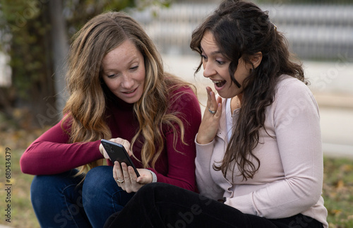 Couple of girls shocked by what they see on smartphone.Online gossip. photo