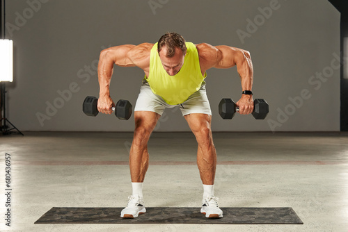 Caucasian athlete spreads his arms with heavy dumbbells to the sides while standing parallel to the floor