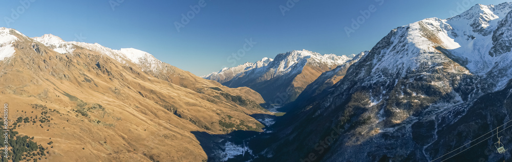Panoramic view of snow-capped mountain peaks in clear sunny weather. Vacation at a ski resort high in the mountains. Clean air in the mountains. Outlines of mountains with icy peaks.