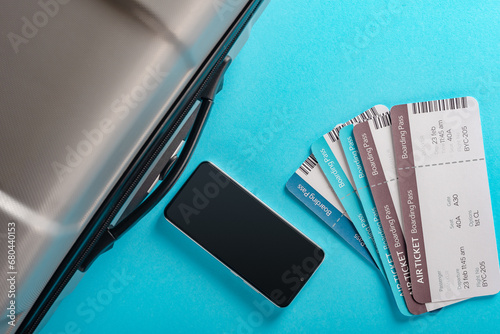 Air tickets, modern smartphone and travel suitcase on blue background