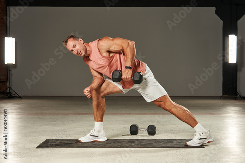 one-arm dumbbell row in a bent-over position with emphasis on the leg by a handsome Caucasian athlete in shorts and a T-shirt. fitness. aerobics. exercises on the mat. physical health photo