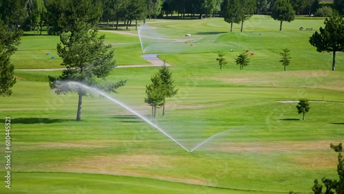 Automatic high-pressure water sprinkler at green golf course watering the grass.