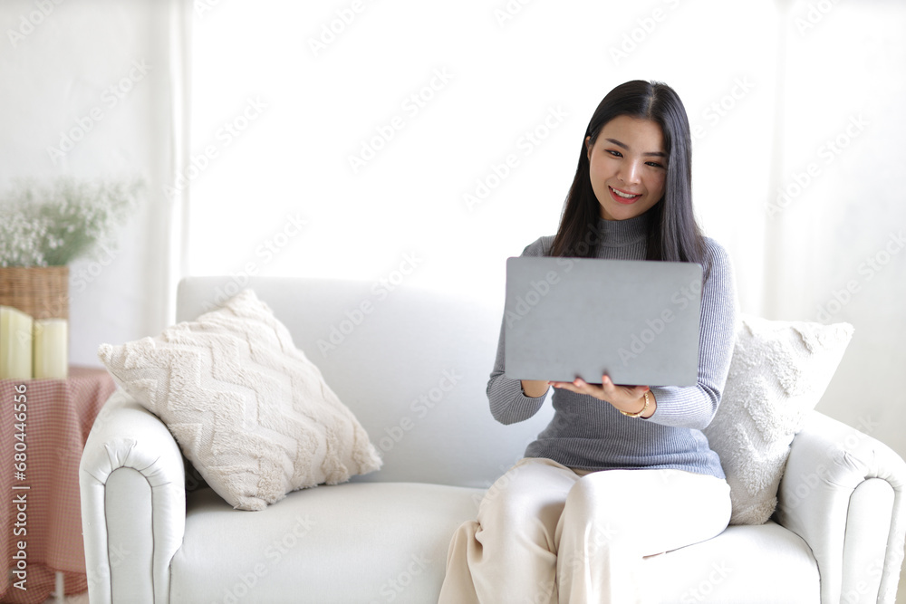 Young asian woman using computer laptop while seated on couch at home. Happy girl relaxing comfortable, using laptop in the living room, spending lazy weekend, watching movie, shopping online. Young asian woman using computer laptop while seated on couch at home. Happy girl relaxing comfortable, using laptop in the living room, spending lazy weekend, watching movie, shopping online.