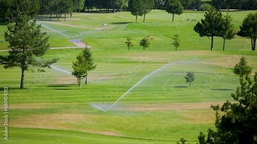 Automatic high-pressure water sprinkler at green golf course watering the grass.