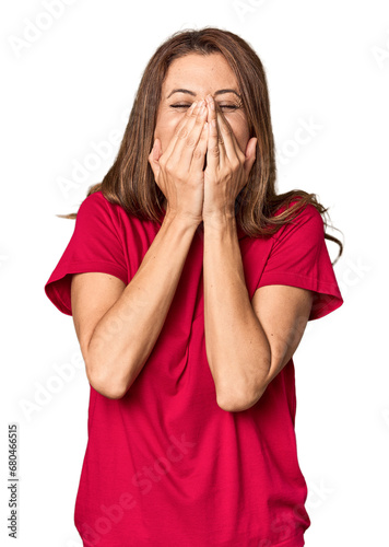 Middle-aged woman portrait in studio setting laughing about something, covering mouth with hands.