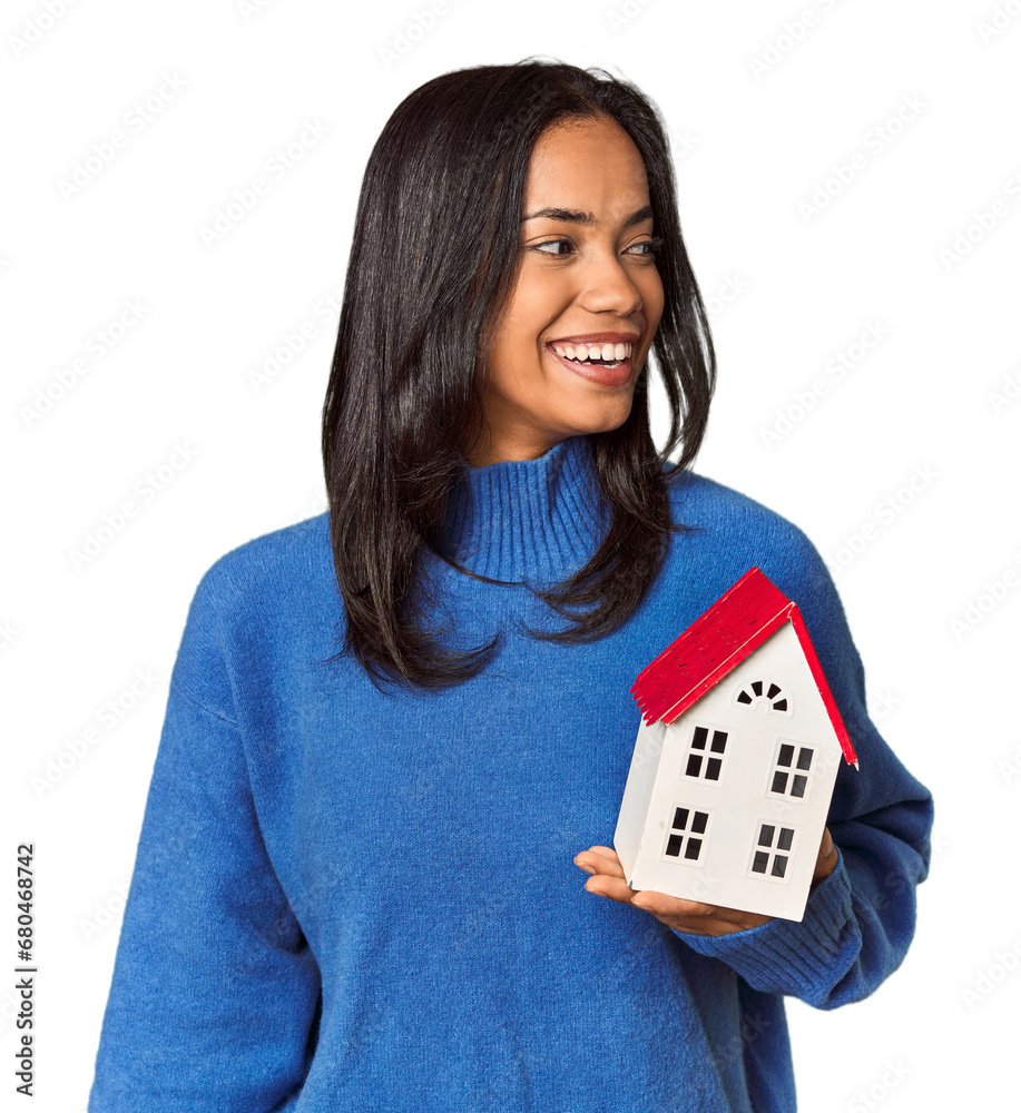 Young Filipina woman holding a miniature house looks aside smiling, cheerful and pleasant. Young Filipina woman holding a miniature house looks aside smiling, cheerful and pleasant.
