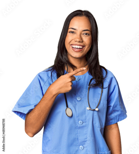 Young Filipina nurse posed in studio smiling and pointing aside, showing something at blank space.