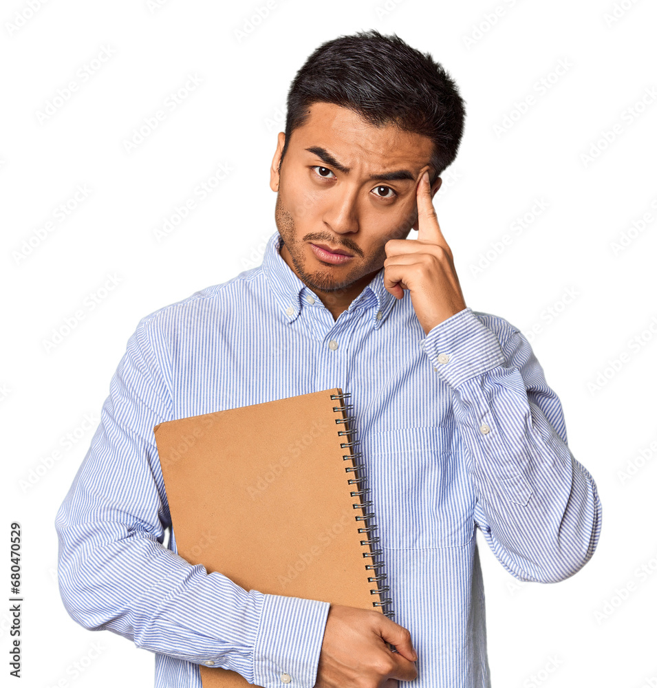 Chinese student with a notebook in studio pointing temple with finger, thinking, focused on a task. Chinese student with a notebook in studio pointing temple with finger, thinking, focused on a task.