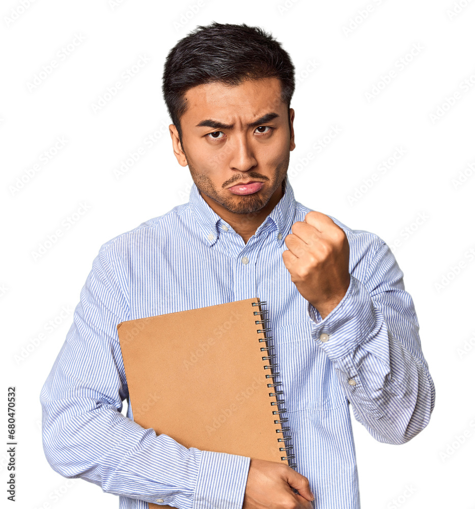 Chinese student with a notebook in studio showing fist to camera, aggressive facial expression. Chinese student with a notebook in studio showing fist to camera, aggressive facial expression.