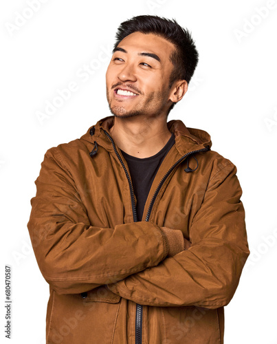 Young Chinese man in studio background smiling confident with crossed arms.