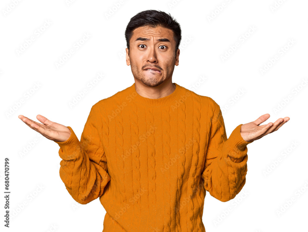 Young Chinese man in studio background confused and doubtful shrugging shoulders to hold a copy space.