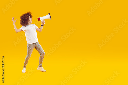 Happy preteen boy shouting into megaphone making announcement. Full length portrait of happy boy in white shirt and jeans holding megaphone screaming into empty space over isolated background
