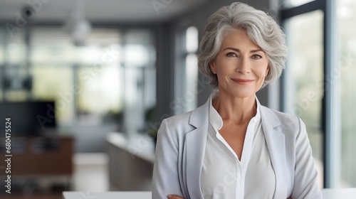 A confident senior businesswoman with gray hair, wearing a smart suit, stands in a modern office setting, representing success and challenging ageism in the corporate world.