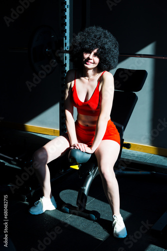 Fototapeta Naklejka Na Ścianę i Meble -  Girl athlete with black curly hair in bright sunlight in the gym.