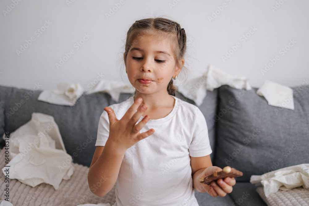 Adorable and beautiful little girl eats chocolate, but it melts in her hands, so the girl licks her fingers. Sweets. Chaos on background. Mess Adorable and beautiful little girl eats chocolate, but it melts in her hands, so the girl licks her fingers. Sweets. Chaos on background. Mess