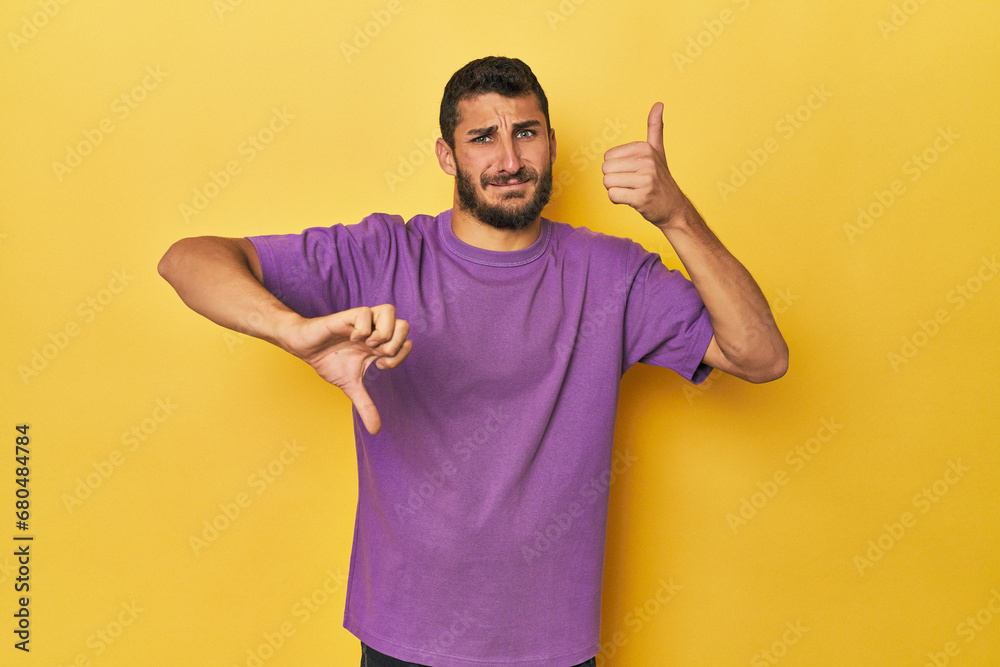 Young Hispanic man on yellow background showing thumbs up and thumbs down, difficult choose concept Young Hispanic man on yellow background showing thumbs up and thumbs down, difficult choose concept