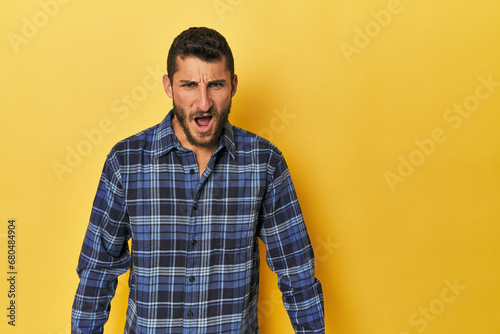 Young Hispanic man on yellow background shouting very angry, rage concept, frustrated.
