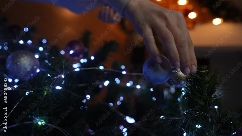 Vertical video. Close-up. A woman hangs a Christmas ball on a Christmas tree and hits it with her finger Vertical video. Close-up. A woman hangs a Christmas ball on a Christmas tree and hits it with her finger