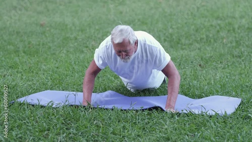 An elderly, gray-haired man with a white sports T-shirt does push-ups in nature, the concept of seniors engaging in sports