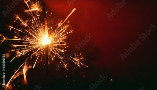 Sparkler burning bright with shiny sparks. Dark red festive background. Happy New Year concept.