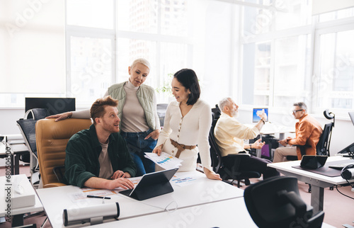 Group of diverse colleagues discussing work at table with laptop and papers in office