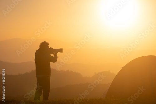 Photographer is taking landscape photo by the tent during overnight camping at the beautiful scenic sunrise over the mountain for outdoor adventure vacation travel
