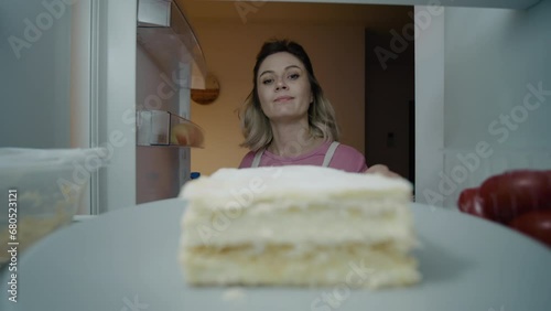 Undecisive pregnant taking the cake out of fridge and putting it back. Pregnant stops herself from eating at night. Pregnancy craving concept. photo