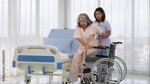 A nurse carries an elderly Asian patient into a wheelchair to take him to get an x-ray of his leg injured in an accident.