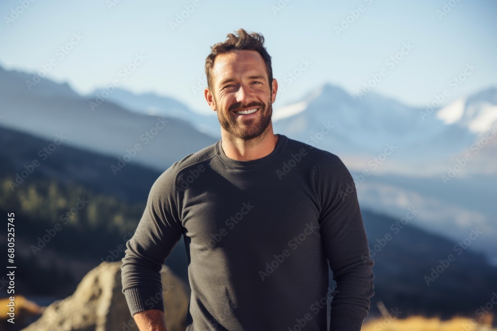 Portrait of a happy man in his 30s showing off a thermal merino wool top against a backdrop of mountain peaks. AI Generation