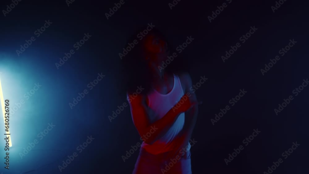Young asian male performer with long hair cheerfully dancing and swinging his hair in a white tank top close up under the red lights on a dark stage. Modern performance with concert light Young asian male performer with long hair cheerfully dancing and swinging his hair in a white tank top close up under the red lights on a dark stage. Modern performance with concert light