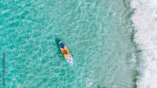 overhead drone view of a person on his stand up paddle board in the sea with green water on the beach with the whitest sand in the world in Jervis Bay, Australia on a daylight morning on vacation