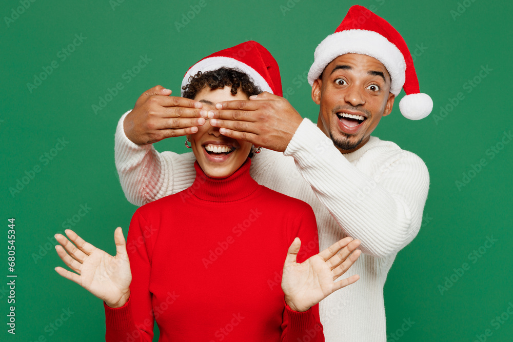Merry young couple man woman wear red casual clothes Santa hat posing close eyes with hands play guess who or hide and seek isolated on plain green background. Happy New Year 2024 Christmas concept. Merry young couple man woman wear red casual clothes Santa hat posing close eyes with hands play guess who or hide and seek isolated on plain green background. Happy New Year 2024 Christmas concept.