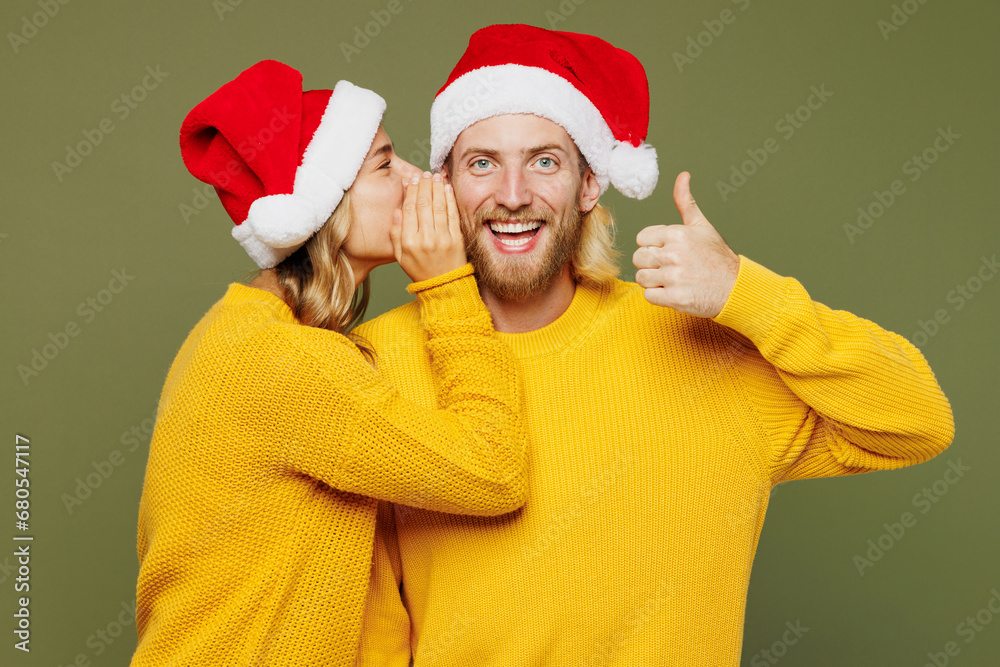 Merry fun young couple two friends man woman wear sweater Santa hat posing whisper gossip tell secret behind his hand sharing news isolated on plain green background. Happy New Year Christmas concept. Merry fun young couple two friends man woman wear sweater Santa hat posing whisper gossip tell secret behind his hand sharing news isolated on plain green background. Happy New Year Christmas concept.