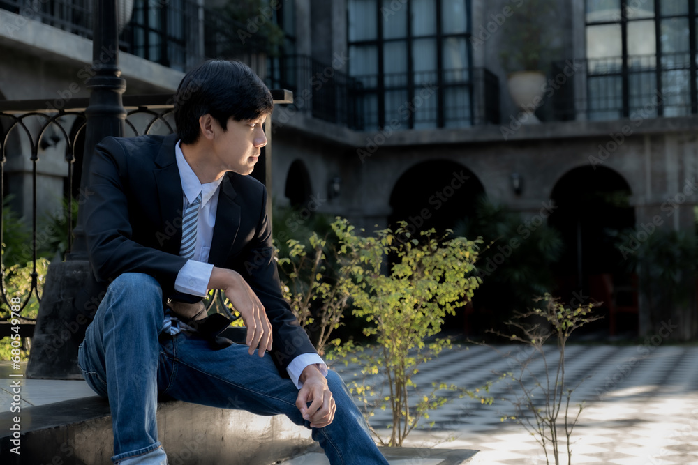 A young businessman sits with a luxurious black building in the background A young businessman sits with a luxurious black building in the background