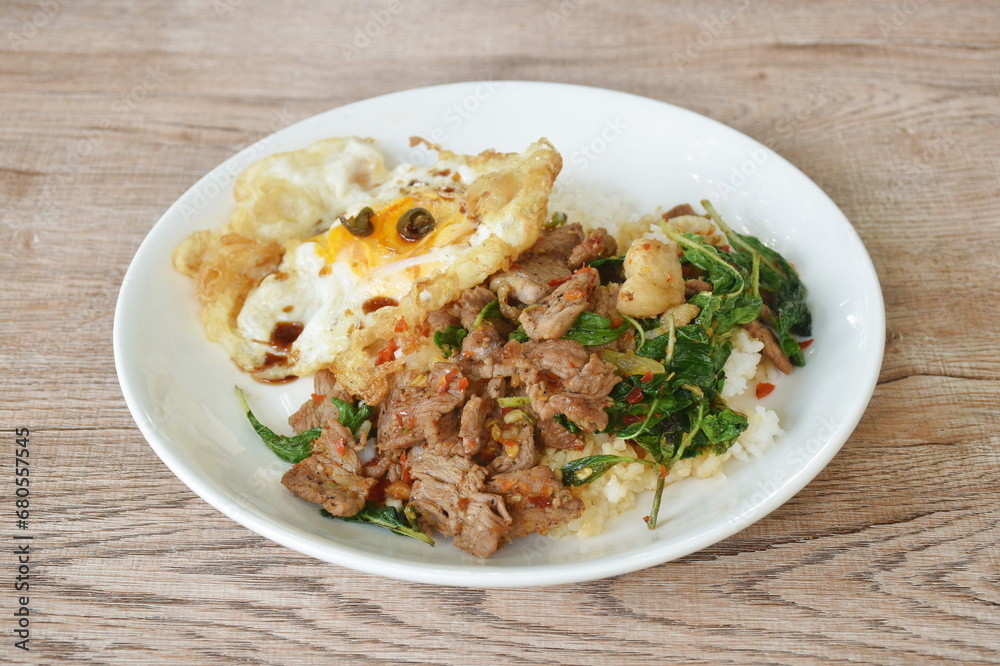 spicy stir fried slice beef meat with basil leaf and chili on rice topping egg in plate spicy stir fried slice beef meat with basil leaf and chili on rice topping egg in plate