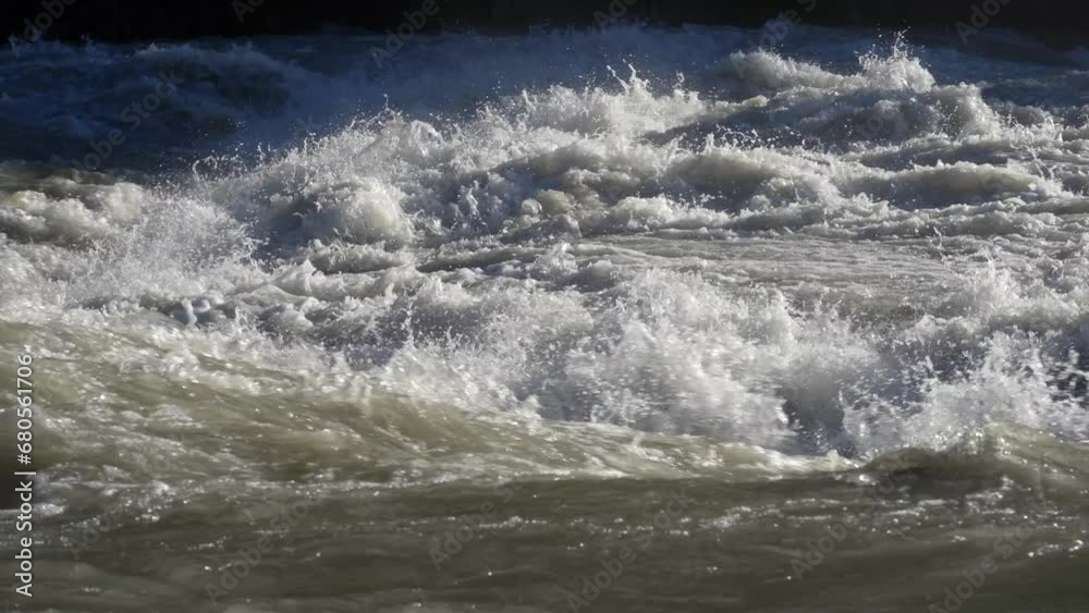 Close-up to the river swollen after heavy rainfall and flood water crashing through valley. The water flows fast from the high valley to the plain. General contest of a river in flood Close-up to the river swollen after heavy rainfall and flood water crashing through valley. The water flows fast from the high valley to the plain. General contest of a river in flood