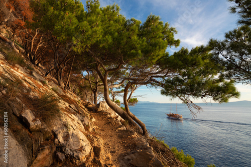 Fototapeta Naklejka Na Ścianę i Meble -  Far view of boat on the sea near the Makarska city, Croatia. Beautiful landscape in Park Osejava near Makarska, Croatia. Gravel path in forest near Adriatic sea.
