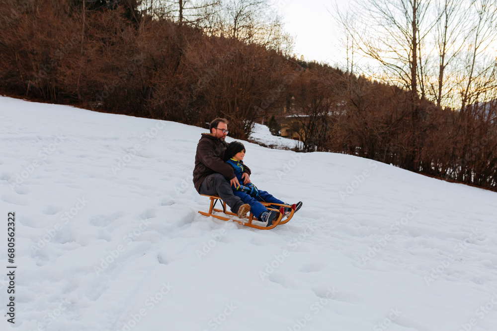 father and child together on wooden sled going down the snowy hill