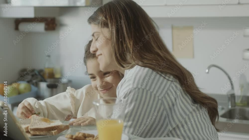 Loving mother talking with adorable little daughter over breakfast at home, then hugging and kissing her Loving mother talking with adorable little daughter over breakfast at home, then hugging and kissing her