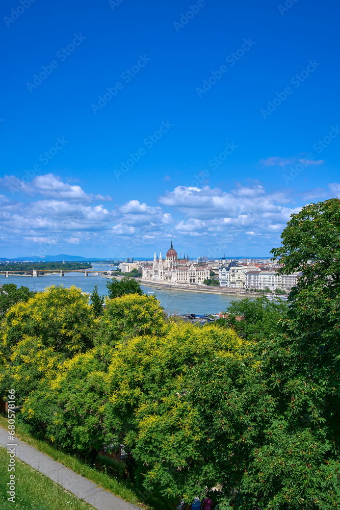 Hungarian parliament building as seen from the hills on a sunny summer day with lush green trees in foreground. Budapest, Hungary.