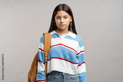 Focused teen student girl with backpack on shoulder isolated studio background. Serious unsmiling joyless young teenager schoolgirl looking at camera. Beginning of academic year, admission to college photo