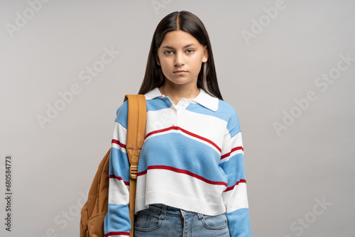 Focused teen student girl with backpack on shoulder isolated studio background. Serious unsmiling joyless young teenager schoolgirl looking at camera. Beginning of academic year, admission to college