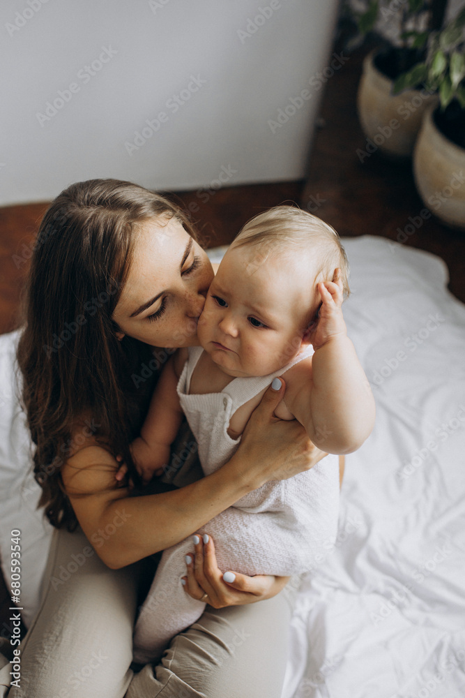 Mother calming her crying baby with a kiss on the cheek in a bedroom Mother calming her crying baby with a kiss on the cheek in a bedroom